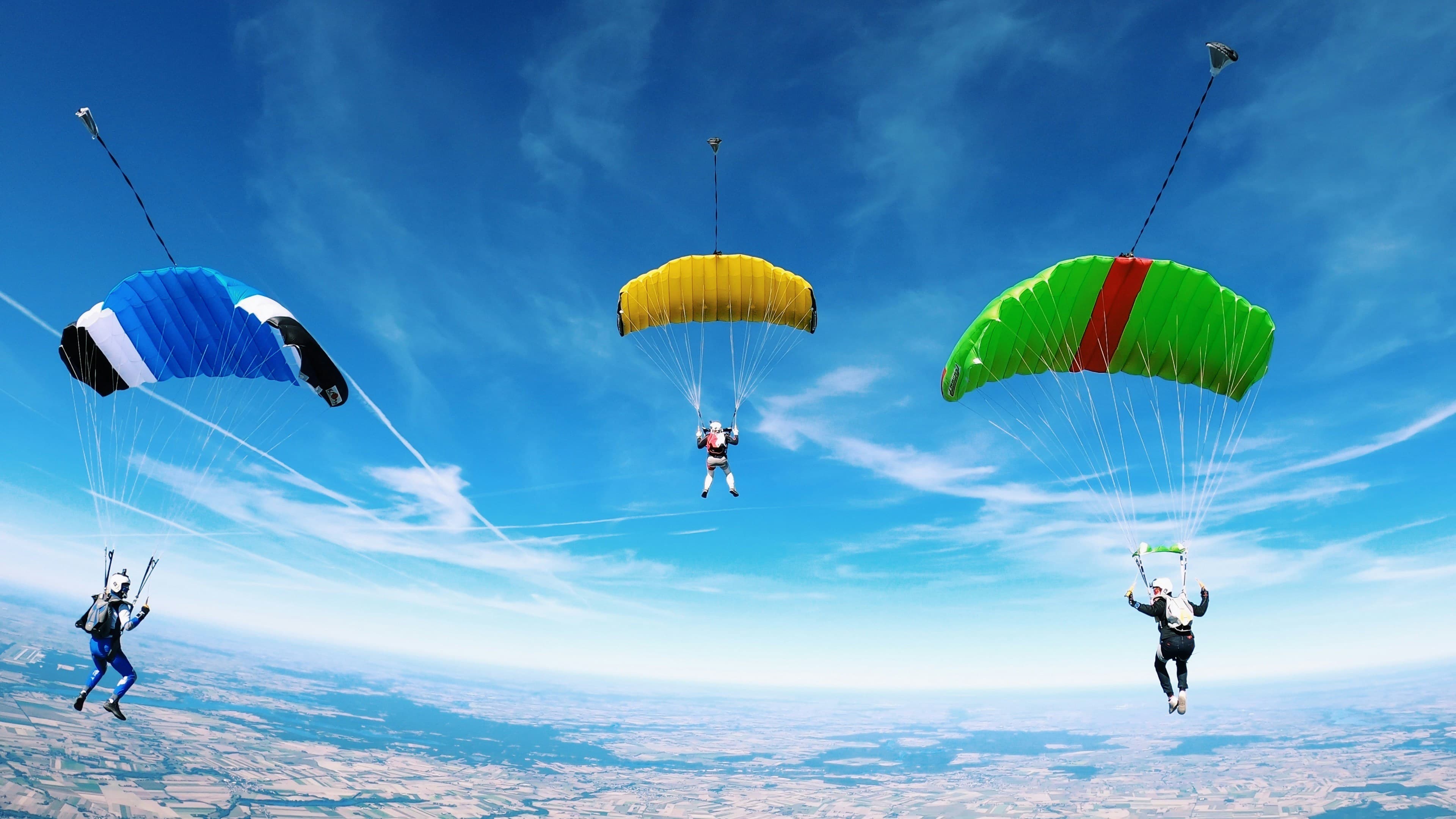 Four skydivers with colorful canopies against a bright blue sky
